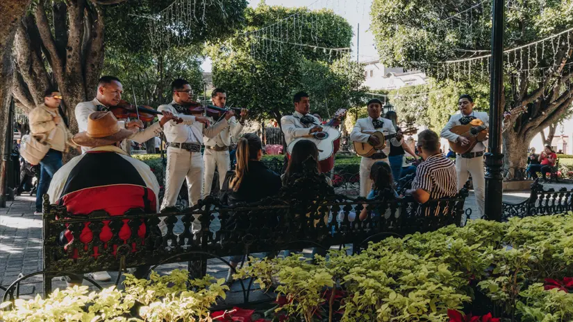 Mexican street band playing music in front of people sitting on benches.